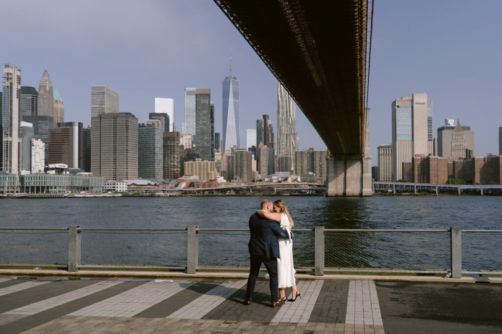 A couple standing close together under a bridge in New York City 