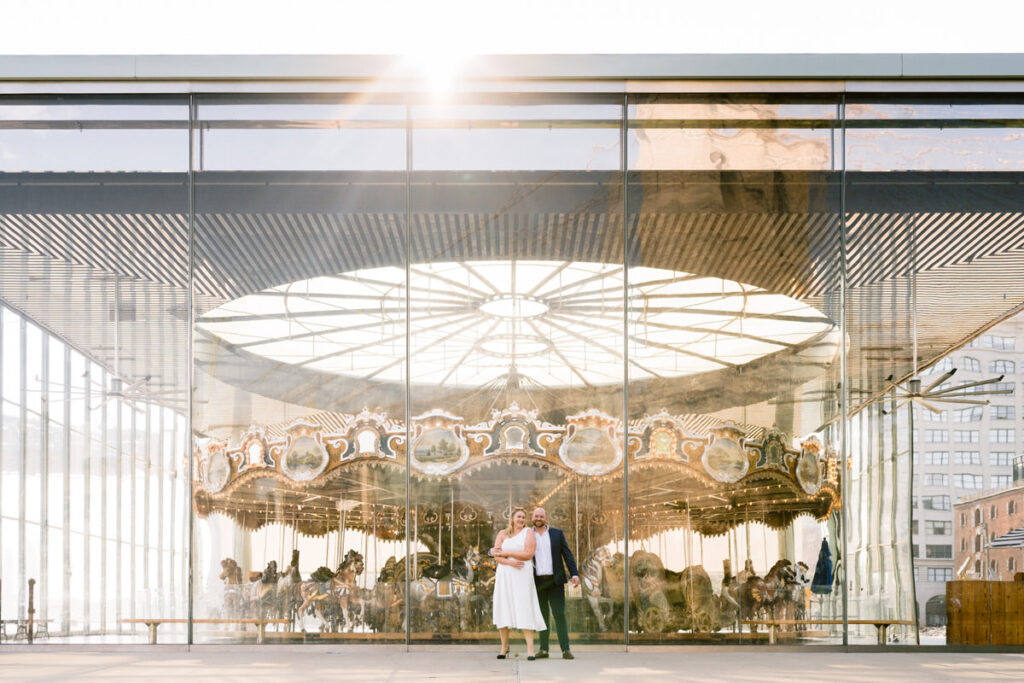 A couple standing together in front of a carousel 