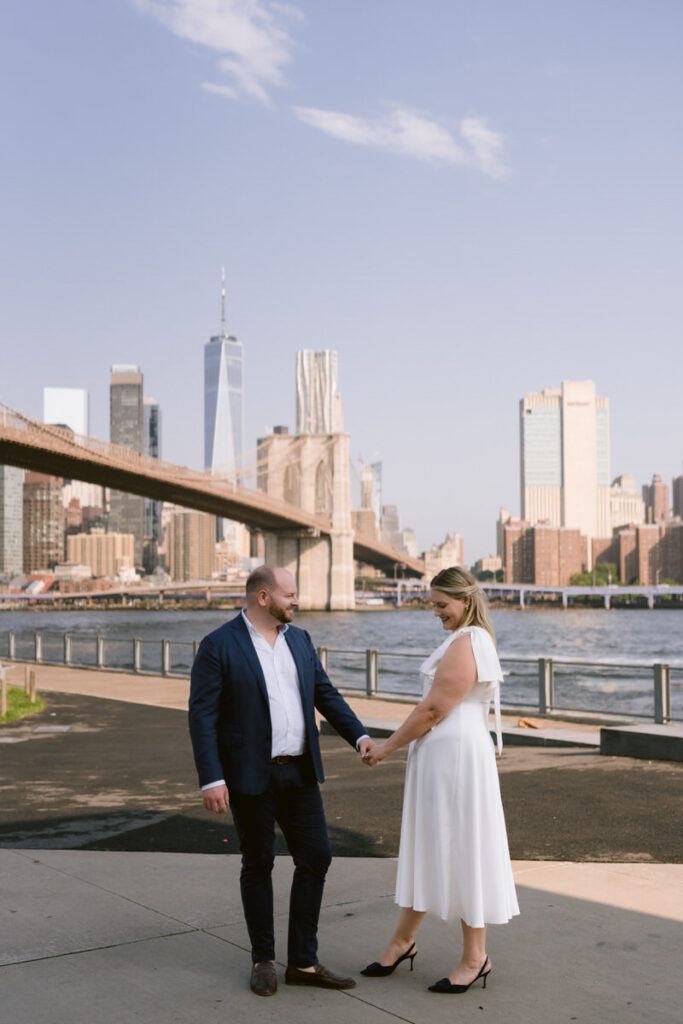 A couple holding hands and smiling together by the water in a city 