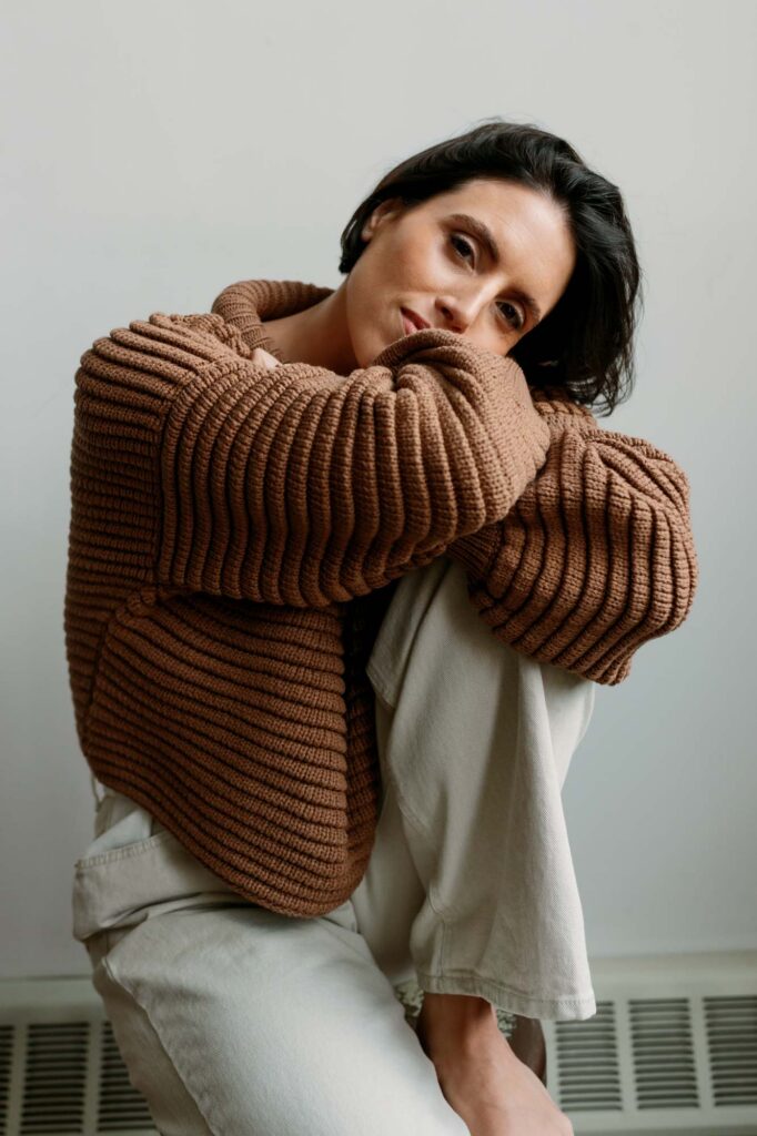 Relaxed portrait of Zay hugging her knee in an oversized camel sweater